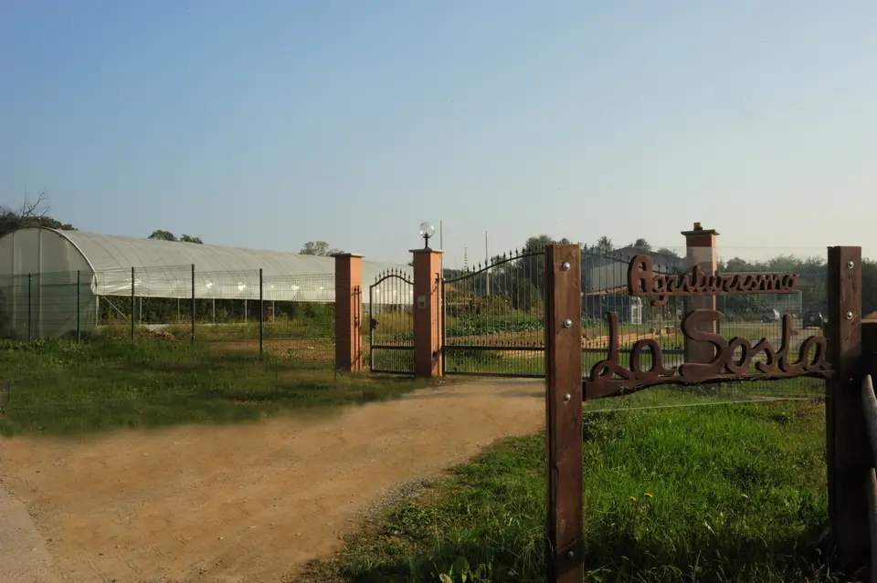 L'insegna in ferro battuto «Agriturismo La Sosta» all'ingresso della cascina, con la serra sullo sfondo